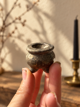 Load image into Gallery viewer, Dark bronze-speckled miniature stone cauldron held between fingers for scale