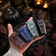 Load image into Gallery viewer, Hand holding four assorted crystal coffin carvings with spooky Halloween decor