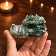 Load image into Gallery viewer, Moss agate dragon head carving held in hand with dark wood and candlelight background