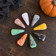 Load image into Gallery viewer, Overhead view of eight assorted crystal raven skull carvings with a pumpkin at the edge.