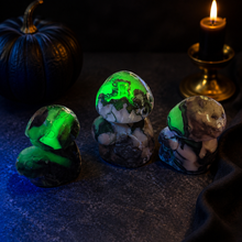 Load image into Gallery viewer, Three Volcano Agate mushroom carvings glowing green under UV light with a black pumpkin and candle
