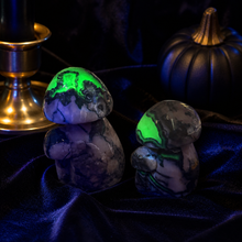 Load image into Gallery viewer, Two Volcano Agate mushroom carvings glowing green under UV light on dark velvet
