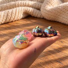 Load image into Gallery viewer, Four rainbow aura pumpkin carvings held in hand for scale, with wood and cream knit background
