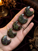 Load image into Gallery viewer, Dragon's blood crescent moon stone carvings displayed in hand with a spooky woodland background
