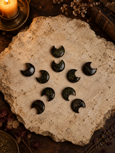 Load image into Gallery viewer, Dragon's blood crescent moon stone carvings arranged overhead in a dark spooky setting
