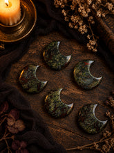 Load image into Gallery viewer, Dragon's Blood Jasper crescent moon carvings on dark wood by candlelight
