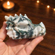 Load image into Gallery viewer, Moss agate dragon head carving held in hand with dark wood and candlelight background

