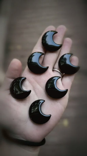 Black obsidian crescent moon carvings shown in hand with a dark atmospheric product-video treatment