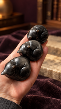 Load image into Gallery viewer, Three silver sheen obsidian sleepy cat carvings resting in a palm for size reference

