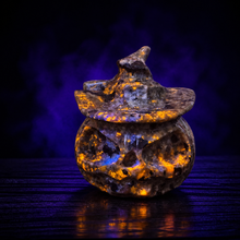 Load image into Gallery viewer, Yooperlite pumpkin with witch hat glowing orange under UV light against a dark violet background
